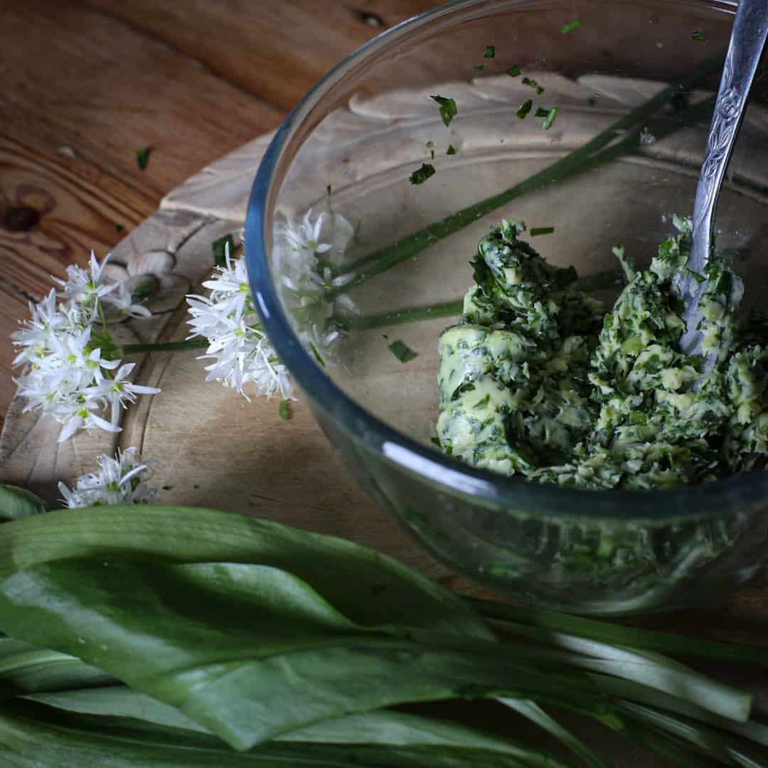 Glass bowl of wild garlic butter on a wooden counter with a bunch of wild ramsons