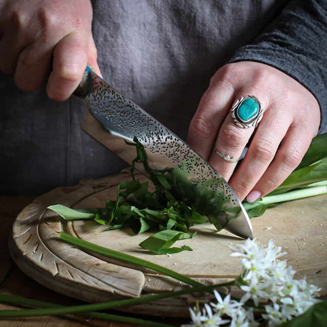 Womans hands chopping wild garlic leaves and flowers on a wooden chopping board