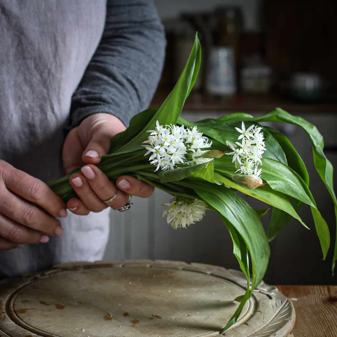 Woman in grey holding a bunch of wild garlic leaves and flowers