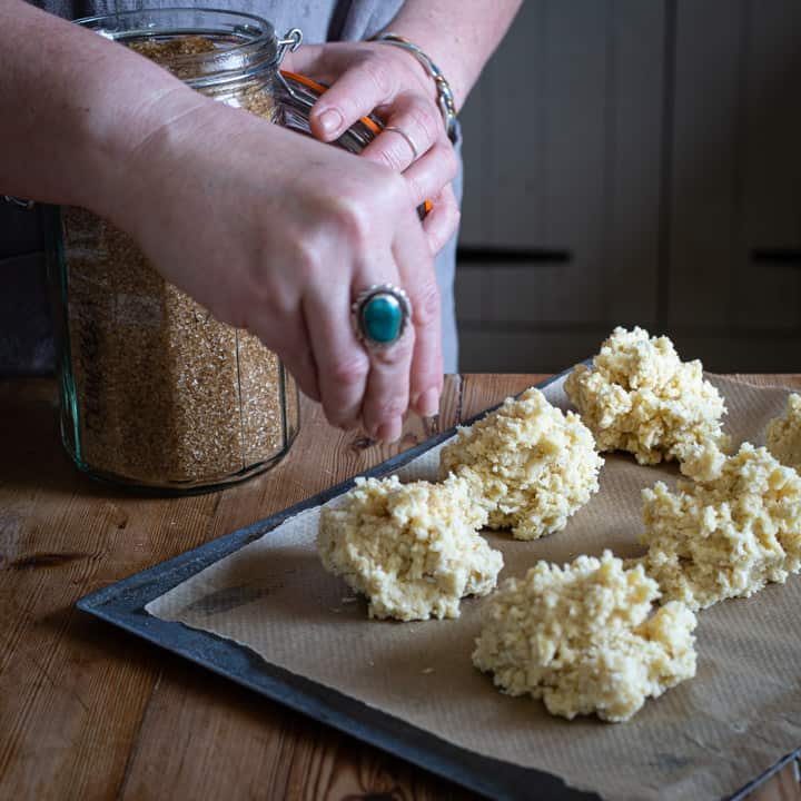 woman in grey sprinkling brown sugar on top of rock cakes dough before baking