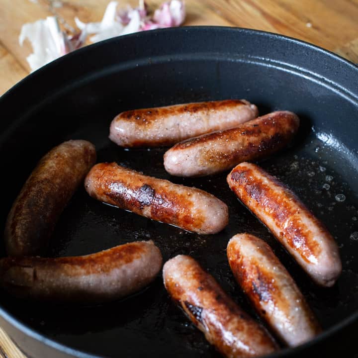 8 browned sausages in a black cast iron pan