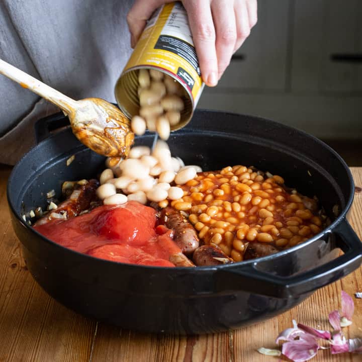 womans hands tipping a can of butter beans into a pan of homemade sausage casserole