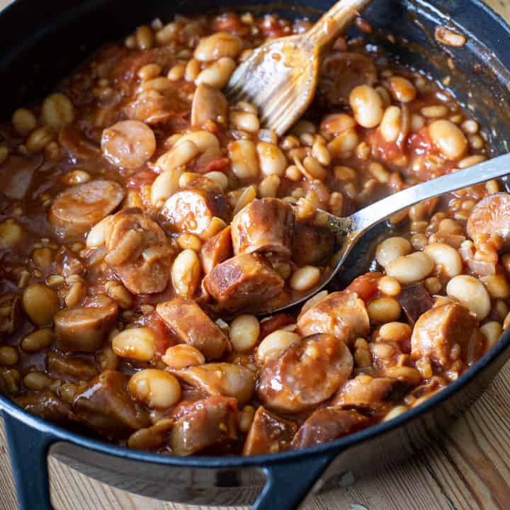 overhead shot inside a black cast iron pan of cowboy casserole with beans and chopped sausages