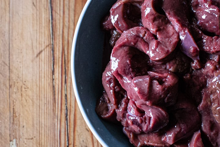 blue bowl on wooden background with ribbons of fresh venison liver inside