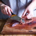 womans hand using knife to remove tough membranes from fresh venison liver to make pate