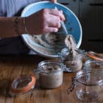 womans hands spooning warm pate from large blue bowl into small glass Kilner jars