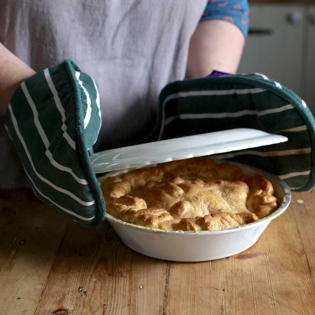 Woman wearing green oven gloves placing a plate over a pie dish filled with a hot rhubarb tart ready to flip it out