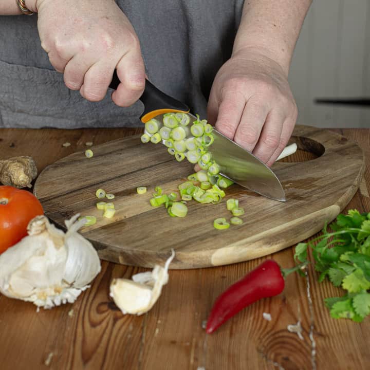 womans hands chopping spring onions on a wooden chopping board