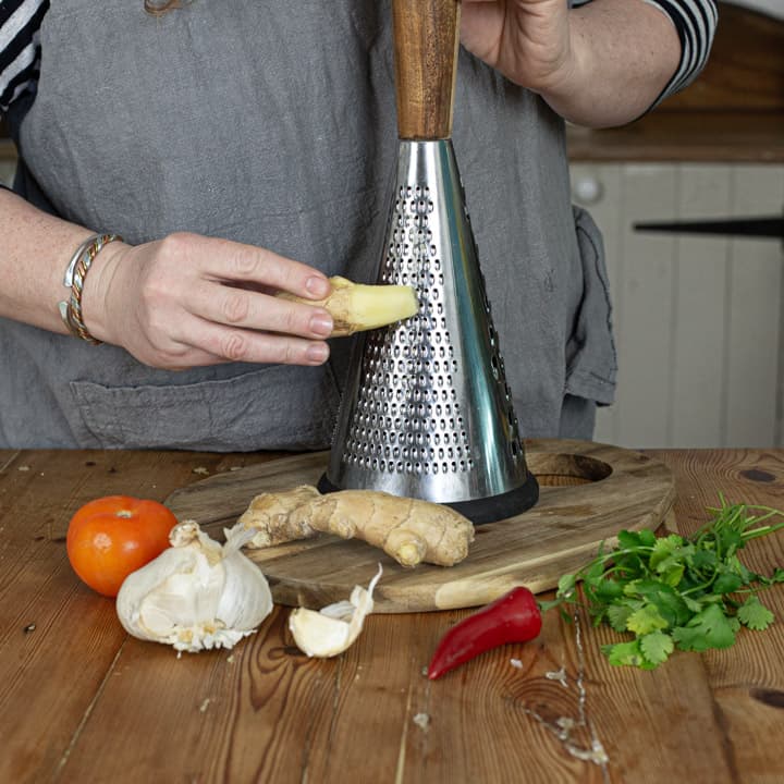 womans hands grating fresh ginger on a wooden chopping board