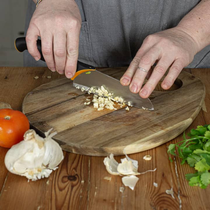 womans hands chopping fresh garlic on a wooden chopping board