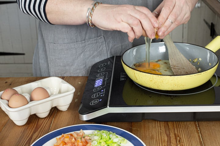 womans hands cracking eggs into a yellow frying pan to make indian eggs