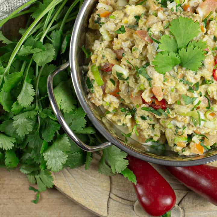 metal bowl of Indian Eggs against a wooden background with fresh coriander and red chillis