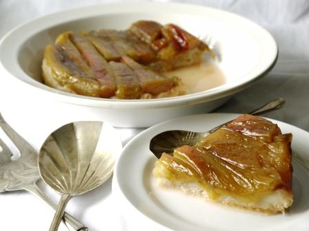 Rhubarb Tarte Tatin on a white serving dish beside a white dessert plate with forks and spoons