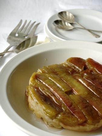 Rhubarb Tarte Tatin on a white serving dish beside a white dessert plate with forks and spoons