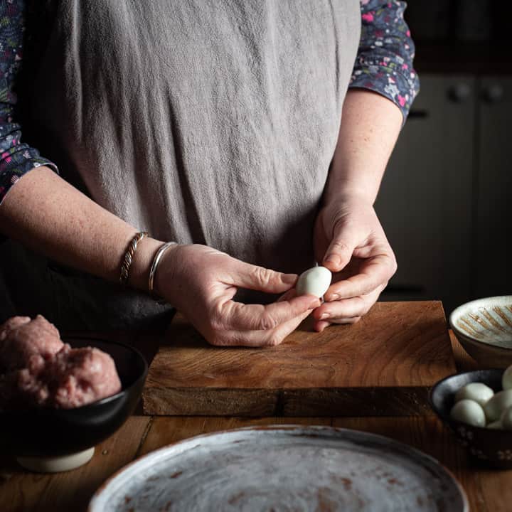 womans hands holding a small quails egg on a rustic wooden kitchen counter