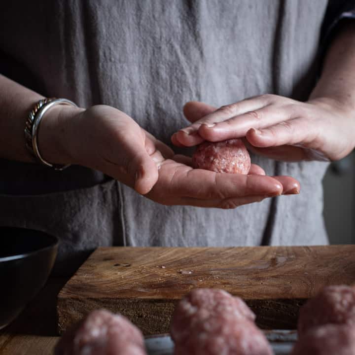 womans hands rolling a scotch egg out in a rustic kitchen setting