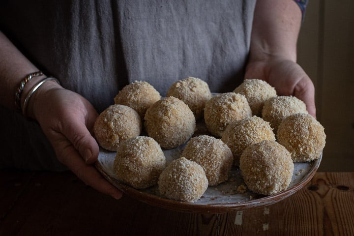 womans hands holding a white plate of homemade mini scotch eggs ready for deep frying