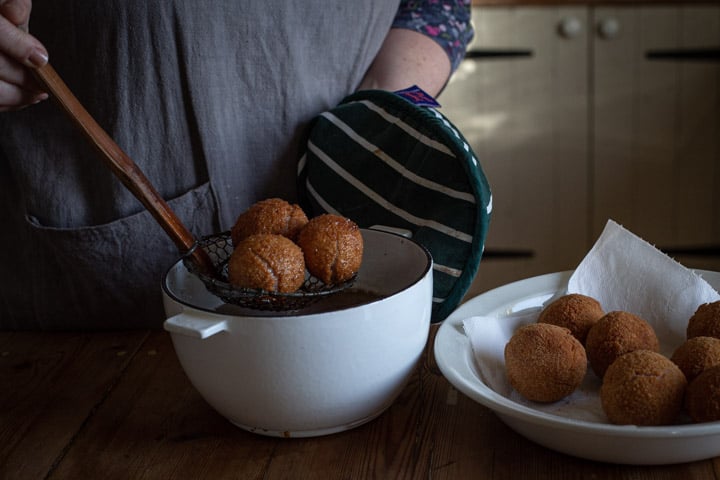 wooden kitchen counter white while pan full of hot oil, and 3 golden scotch eggs being lifted out with a spoon