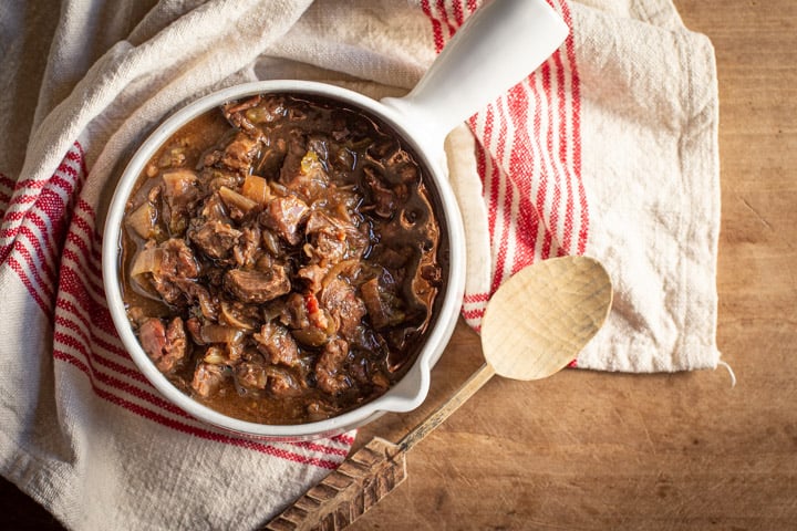 beef and ale stew in white pot with wooden background and wooden spoon