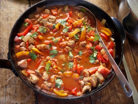 Paprika Pork Fricassee in a large skillet with a serving spoon on a wooden table