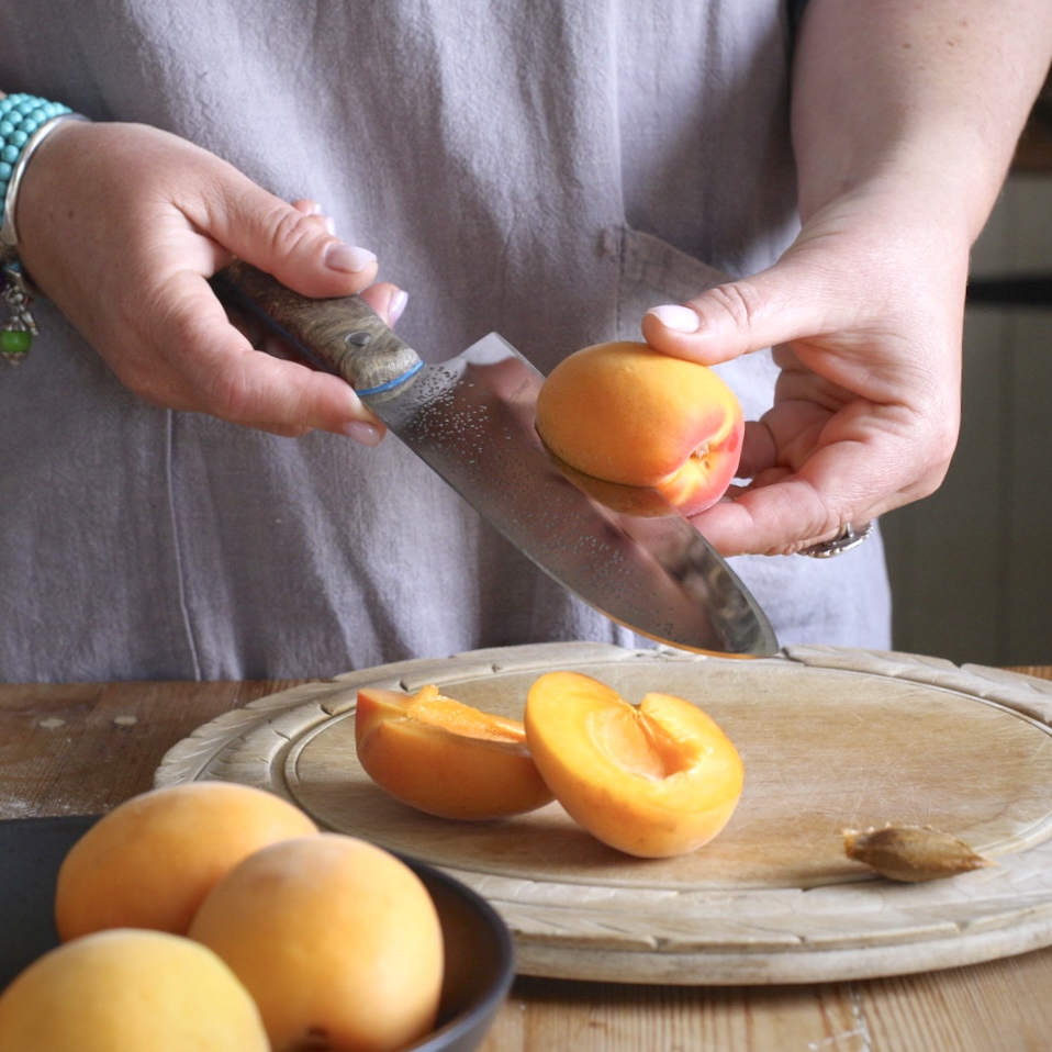 Woman in grey slicing open an apricot with a large silver knife