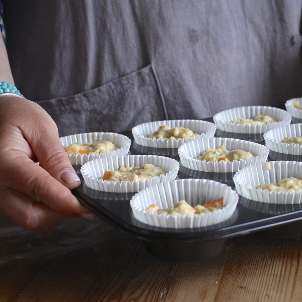 Woman in grey holding a muffin tray filled with muffin batter in a white paper cases ready to go in teh oven