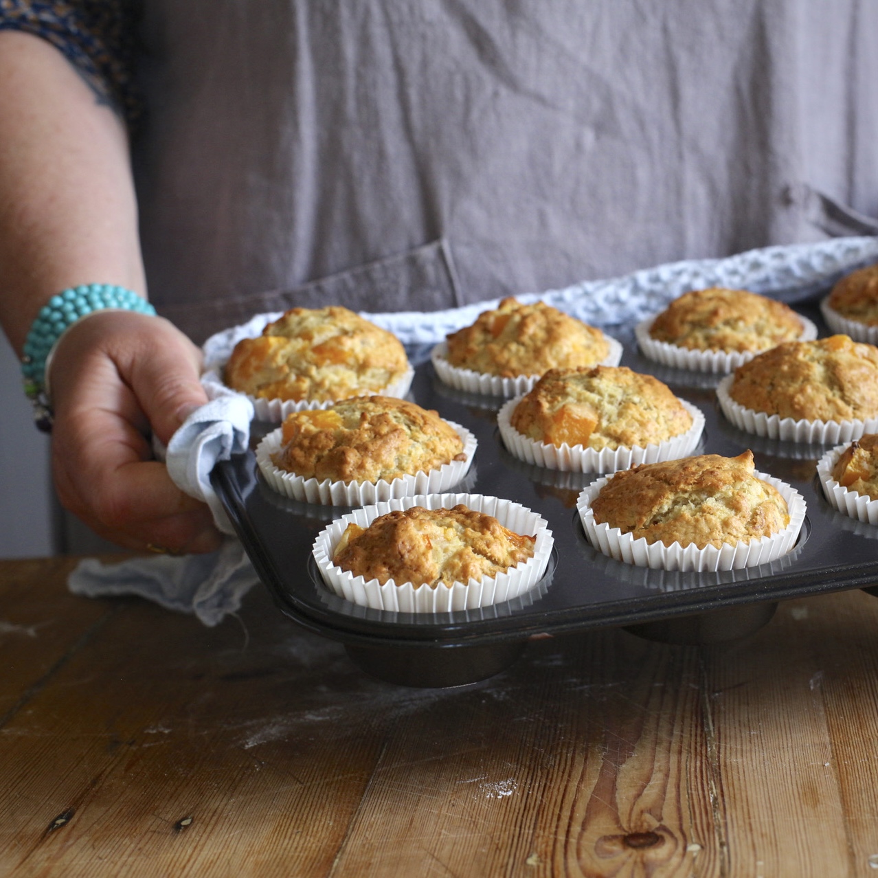 Woman in grey holding a hot muffin tin filled with gorgeous golden muffins 