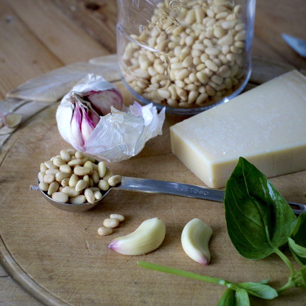 Wooden board with garlic, pinch nuts, basil leaves and Parmesan cheese on