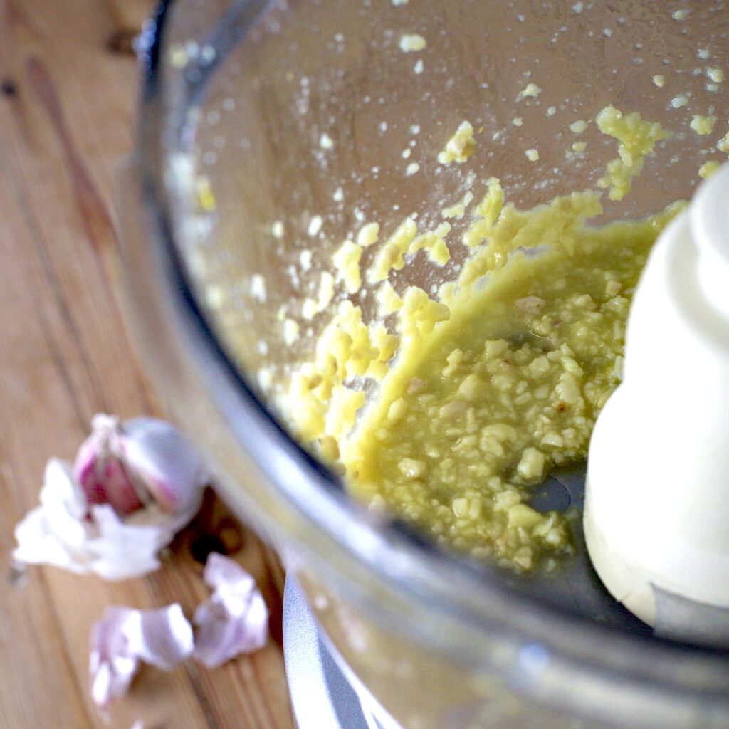 Inside shot of a food processor bowl with garlic, oil and Parmesan cheese 