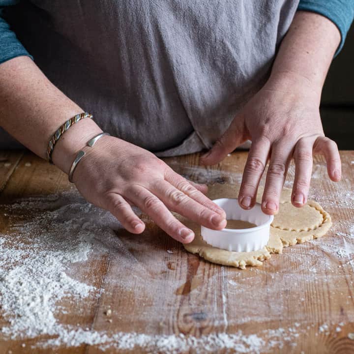 womans hands cutting out cookies from rolled out dough on a wooden kitchen counter