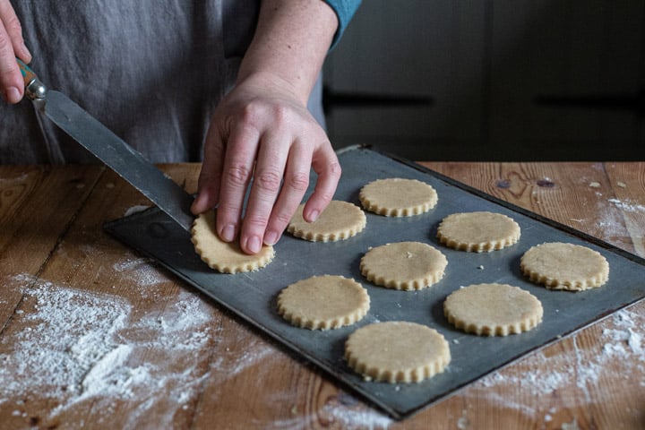 womans hands placing a circle of cookie dough on a silver baking sheet with a palette knife