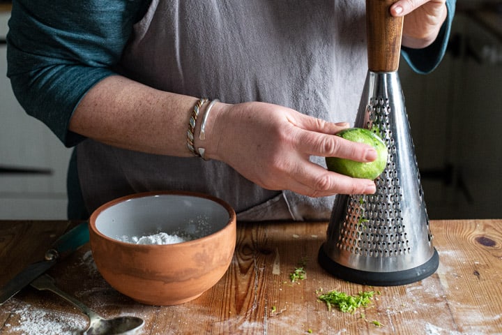 womans hands grating a lime on a wooden kitchen counter