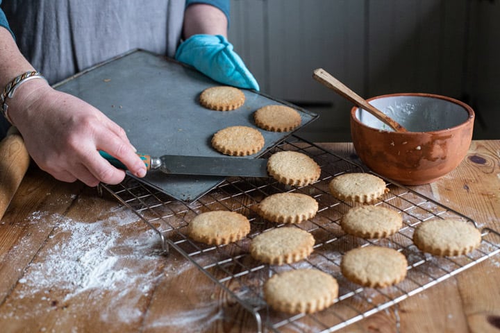 womans hands moving hot freshly baked cookies from a baking sheet onto a wire cooling rack