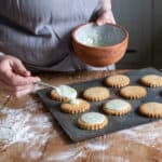 womans hands spooning icing onto fresh cookies on a baking sheet