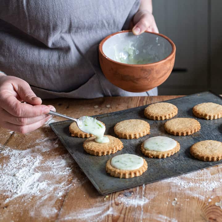 womans hands spooning icing onto fresh cookies on a baking sheet