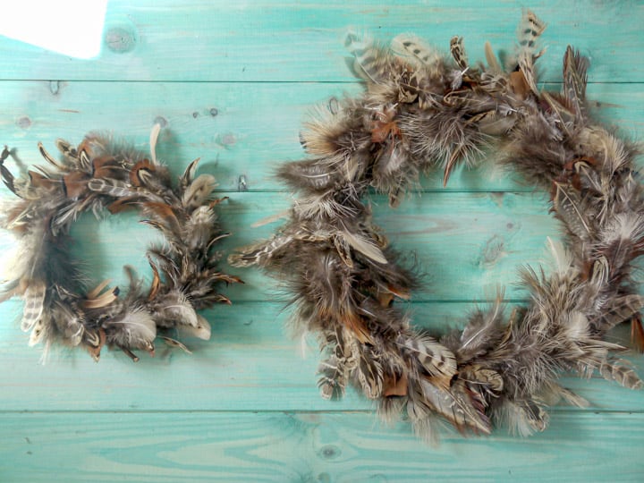 two hand made pheasant feather wreaths against a blue wooden background