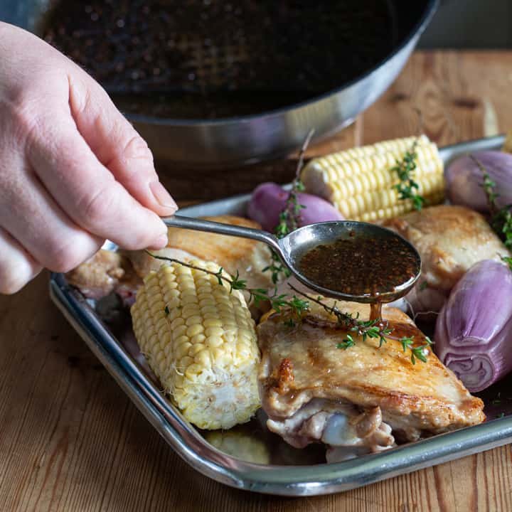 womans hand spooning a honey and mustard dressing over a tray of chicken and vegetables
