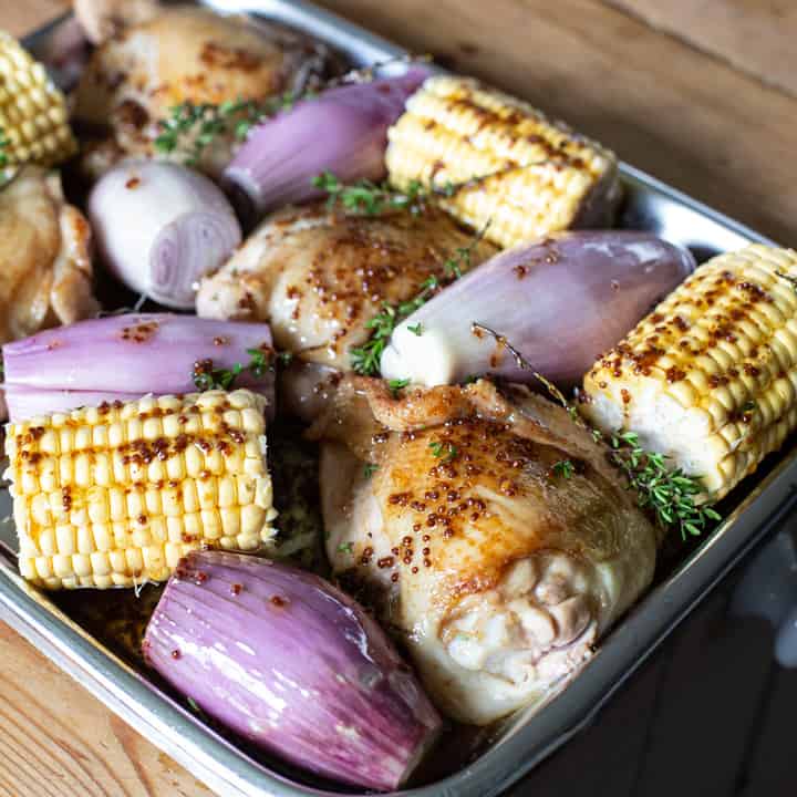 silver tray of chicken thighs, purple shallots and pieces of corn with a mustard dressing ready to go in the oven