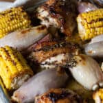 inside of a baking tin of oven baked corn, shallots and chicken thighs