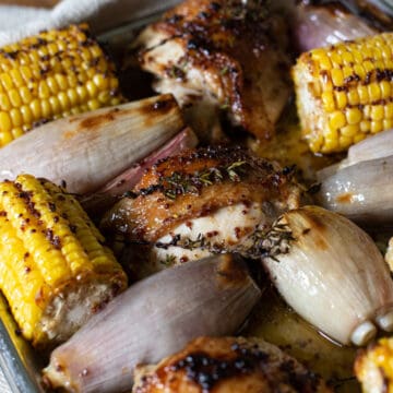 inside of a baking tin of oven baked corn, shallots and chicken thighs