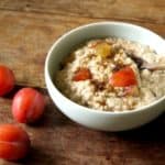 A pretty bowl of plum and cinnamon porridge with brown sugar sprinkled on top.