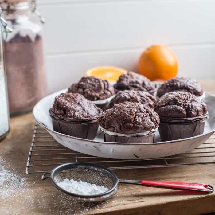 White plate with 7 chocolate orange muffins on, surrounded by baking items