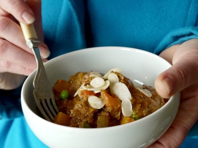Hands holding a white bowl of Lamb, Butternut Squash and Apricot Tagine and a fork