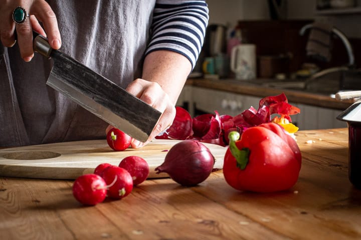 womans hands chopping radishes on a woodne board in a rustic kitchen setting