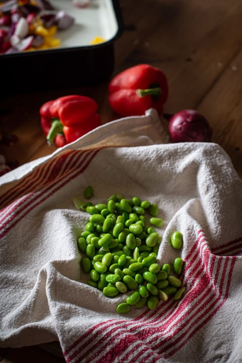 white and red cloth draining defrosted edamame beans in a rustic kitchen setting