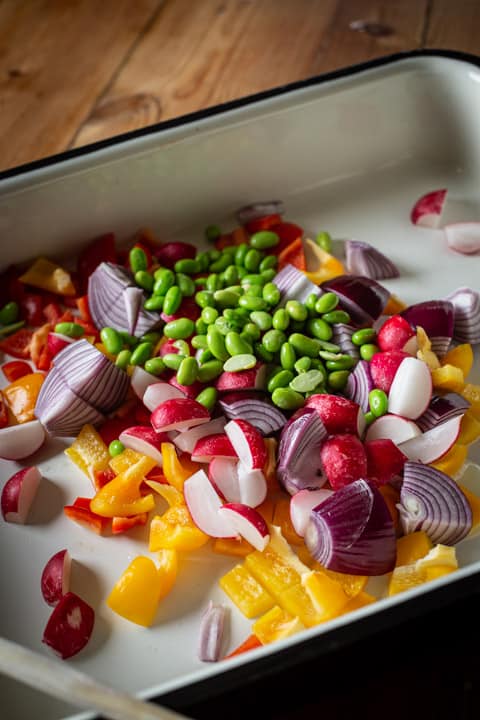 inside of a large baking tin show brightly coloured vegetables about to be roasted