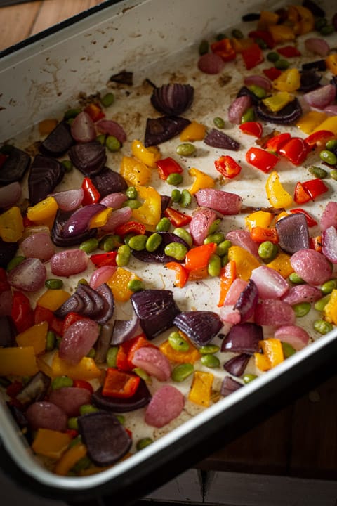 inside of a large baking tin show brightly coloured vegetables that have been roasted