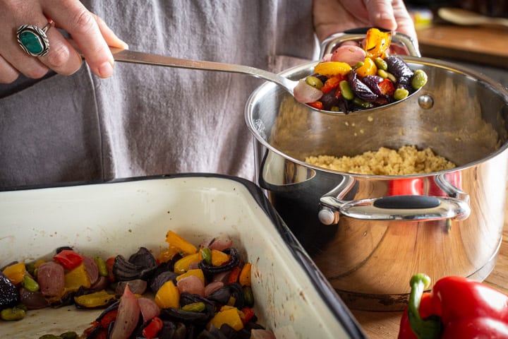 womans hands spooning roast vegetables into a pan of freshly cooked couscous