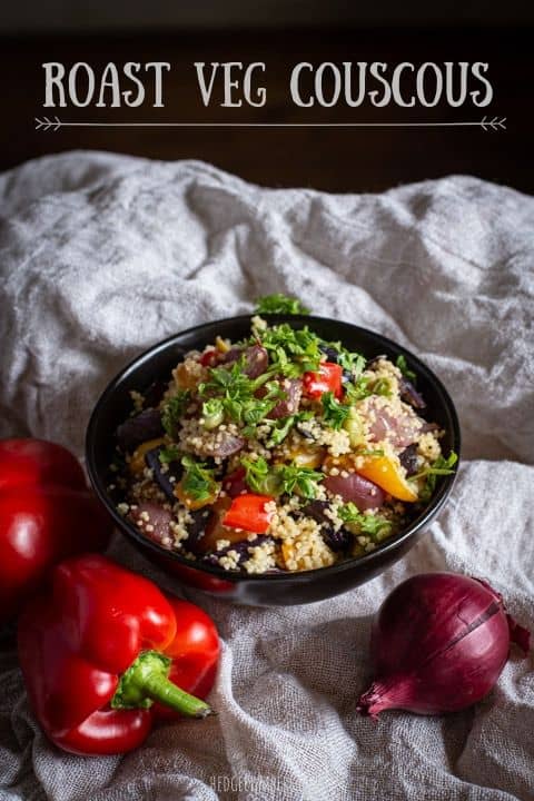 black bowl filled with colourful roast veg couscous against a natural fabric background with fresh veggies
