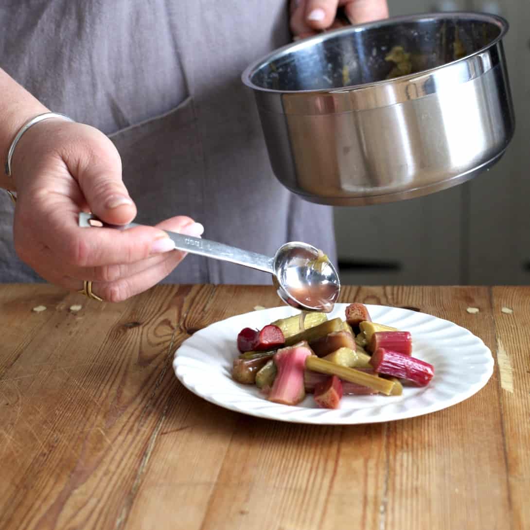 Woman spooning rhubarb juice from a silver saucepan onto a white plate of poached rhubarb 
